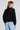 Back view of a woman wearing the Saltwater Luxe Aden Black Sweater on a neutral background
