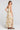 Back view of a woman wearing the Saltwater Luxe  Arosa Midi Dress in Fawn on a neutral background looking over one shoulder