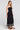 Side angle view of a woman wearing the Saltwater Luxe Jackstin Black Midi Dress on a neutral background
