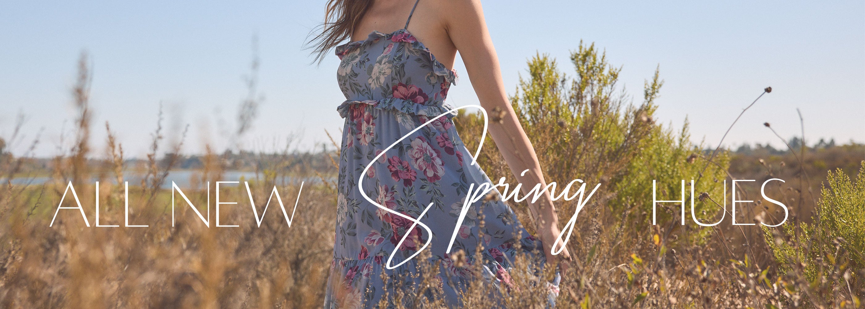 Woman in a floral dress standing in a field with 'All New Spring Hues' text overlay.