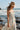 Side angle view of a woman wearing the Saltwater Luxe Medina Midi Dress in Pearl on the beach