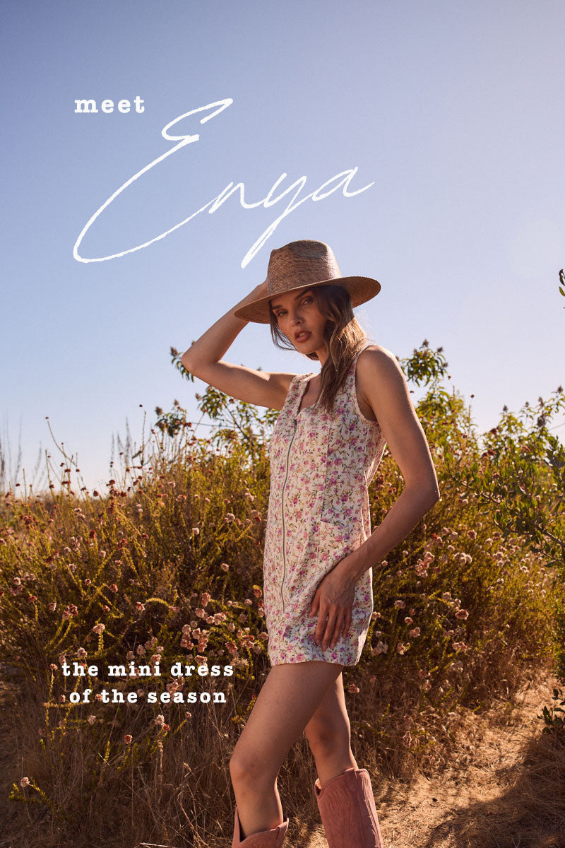 Woman in a floral dress and hat standing in a field with 'Enya' branding