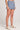 Side angle view of a woman wearing the Saltwater Luxe Pull On Worn Blue Shorts on a neutral background