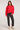 Full body view of woman wearing the Saltwater Luxe Charmer red Sweater with white heart patterns and black jeans and white sneakers on a plain background