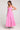 Side full body view of a woman wearing the Saltwater Luxe pink Hayley Midi Dress with a slit on a plain background