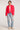Full body view of woman wearing the Saltwater Luxe Brenwood Jacket in Vintage Red with white accents layered over a white shirt and blue jeans on a light gray background