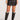 Front view of woman wearing the Saltwater Luxe black Zerra Mini Skirt with black knee-high boots on a plain background