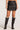 Front view of woman wearing the Saltwater Luxe black Zerra Mini Skirt with black knee-high boots on a plain background