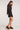 Full body side view of woman wearing the Saltwater Luxe Verra Mini Dress in black polka dot with long sleeves and black sandals on a white background
