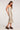 Side view of woman wearing the Saltwater Luxe Oaklie Champagne Midi Dress in gold with black shoes on a white background