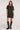 Full body front view of woman wearing the Saltwater Luxe Kove Mini Dress in Black with patterned details and black boots on a white background