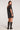 Full body back view of woman wearing the Saltwater Luxe Kove Mini Dress in Black with patterned details and black boots on a white background