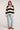 Full body view of woman wearing the Saltwater Luxe Emberr Sweater in stone with black stripes paired with light wash jeans and leopard print sneakers on a white background