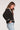 Side view of woman wearing the Saltwater Luxe Joss Sweater a black knit cardigan with decorative patterns and blue jeans on a white background