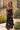 Woman wearing the black Saltwater Luxe Hariette Midi Dress standing outdoors with greenery around
