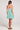 Back full body view of a woman wearing the green and white striped Saltwater Luxe Genevieve Mini Dress on a plain background