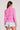 Back view of a woman wearing the Saltwater Luxe pink Amorette Magnolia Sweater and denim shorts on a plain background