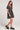 Side view of a woman wearing the Saltwater Luxe black floral Cecillia Mini Dress with black shoes on a white background