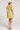 Back view of a woman wearing the Saltwater Luxe green Eldoris Willow Mini Dress with beige boots and a white hat on a plain background
