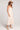 Side view of a woman wearing the Saltwater Luxe Camrie Midi Dress in beige and straw hat on a plain background