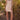 Woman wearing the Saltwater Luxe white Deliah Salt Mini Dress and pink boots standing in a natural setting with greenery