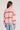 Back view of a woman wearing the Saltwater Luxe pink patterned Jossie Latte Sweater and light blue jeans on a plain background
