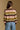 Model wearing the Saltwater Luxe Kaye Sweater multi striped V-neck sweater in brown, cream and olive, back view