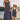 A woman and a young girl wearing matching navy blue and white vertically striped pinafore dresses, standing outdoors by a lake with a railing behind them