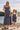A woman and a young girl wearing matching navy blue and white vertically striped pinafore dresses, standing outdoors by a lake with a railing behind them
