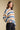 Side angle view of a woman wearing the Saltwater Luxe Mimi Sweater on a neutral background with hand on hem