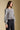 Side view of a woman wearing the Saltwater Luxe Brielle Top on a neutral background with arms at sides and pants