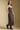 Side angle view of a woman wearing the Saltwater Luxe  Enza Midi Dress on a neutral background with hand in pocket