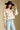 Side angle view of a woman wearing the Saltwater Luxe  Fiorra Sweater on a neutral background with hand on brim of hat