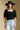 Front view of a woman wearing the Saltwater Luxe Lewis Top on a neutral background with black hat