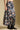 Side angle view of a woman wearing the Saltwater Luxe Maud Midi Floral Skirt on a neutral background with boots and hands at sides
