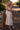 Front view of a woman wearing the Saltwater Luxe Peni Midi Dress on a woodland trail leaning on a post