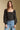Front  view of a woman wearing the Saltwater Luxe on a neutral background with bluejeans and hands at sides