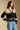 Side angle view of a woman wearing the Saltwater Luxe Scarlit Sweater on a neutral background with hand on hip