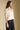 Side view of a woman wearing the Saltwater Luxe Stacia Top on a neutral background with black pants