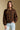 Front view of a woman wearing the Saltwater Luxe  Xenia Chocolate Sweater on a neutral background with hand in pocket