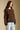 Side angle view of a woman wearing the Saltwater Luxe  Xenia Chocolate Sweater on a neutral background with bluejeans