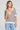 Front view of a woman wearing the Saltwater Luxe Siera Natural Top on a neutral background with her hand at her collar 