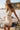 Side angle view of a woman wearing the Saltwater Luxe Waverlee Mini Dress in Natural on the beach