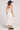Back view of a woman wearing the Saltwater Luxe Woven Ecru Tank Midi Dress on a neutral background