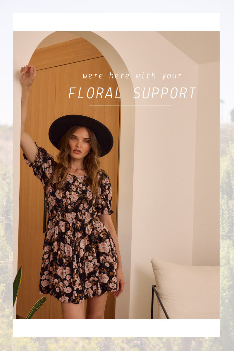 Woman in a floral dress and hat standing in front of a wooden door with text 'Floral Support'.